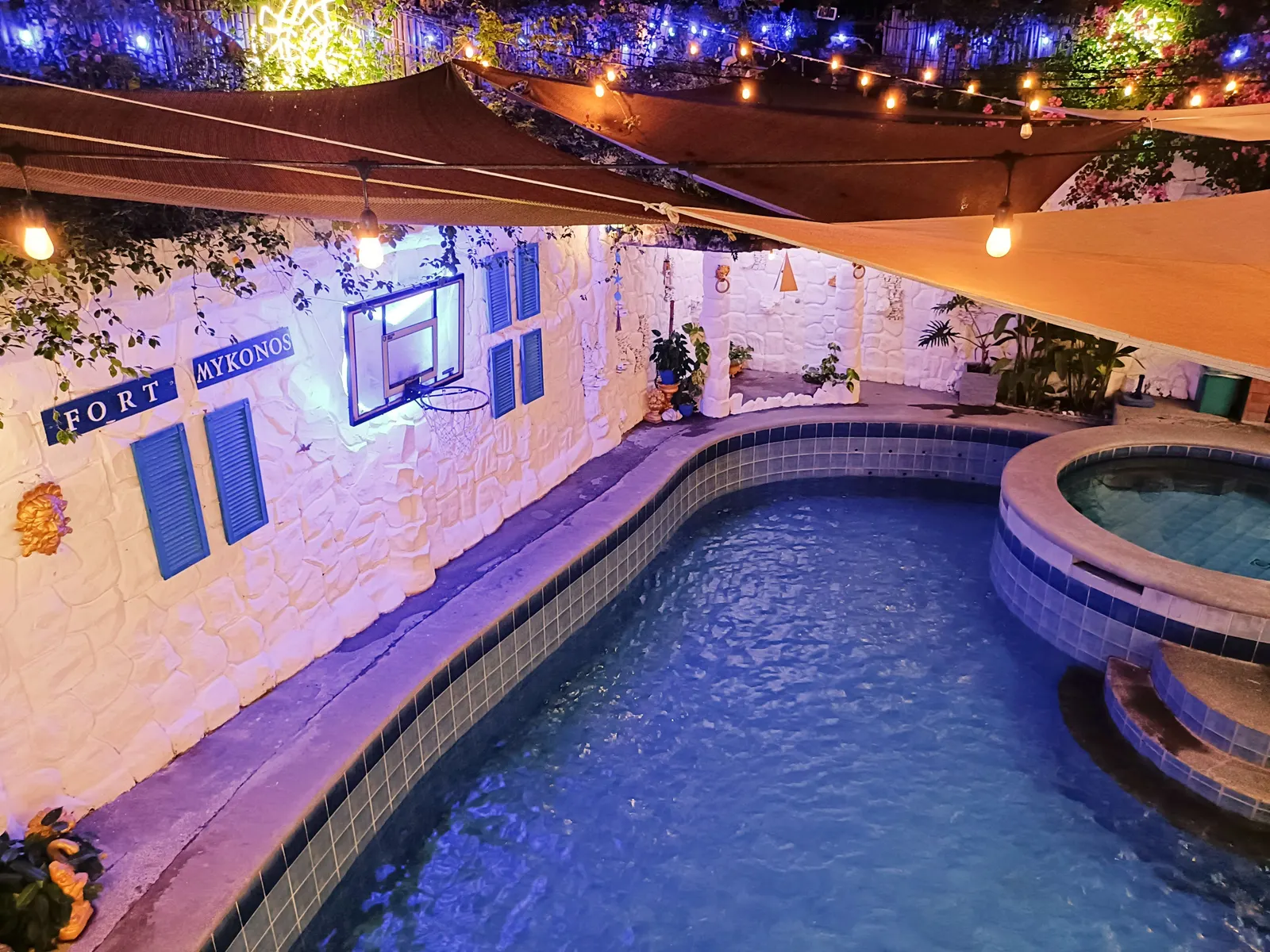 The same pools at night under string lights, beside the whitewashed Fort Mykonos wall